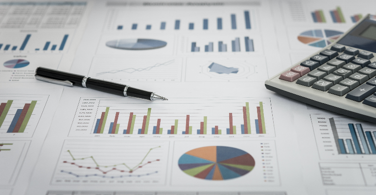 Image of a pen and a calculator sitting on pieces of paper that have charts and graphs